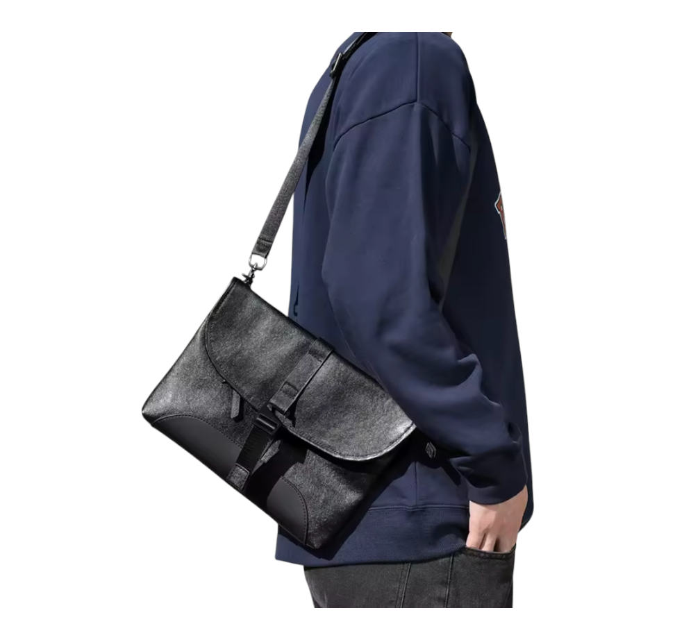 Person wearing a navy blue jacket with a black leather bag over one shoulder on a white background