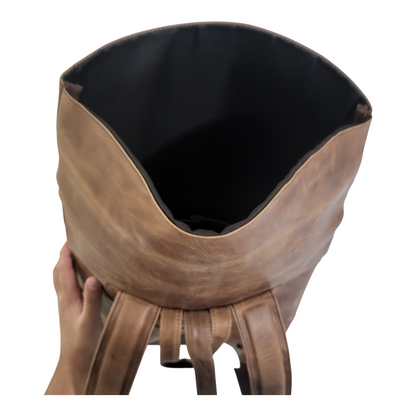 Brown leather backpack with black interior held by a hand on a white background