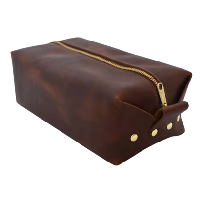 Left side view of a brown leather toiletry bag with gold zipper and studs on a white background